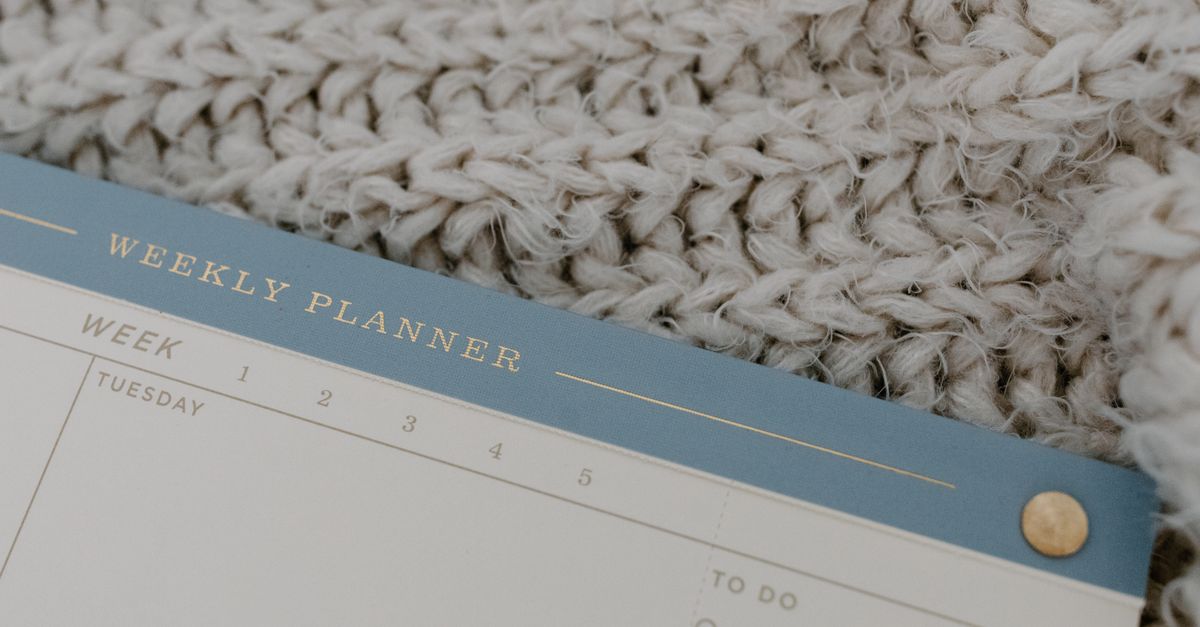 A weekly planner rests on a knitted fabric, providing a cozy vibe for planning.